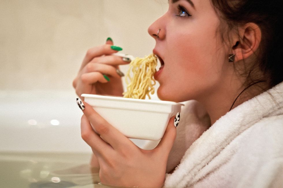 woman holding white bowl with yellow noodles she eats