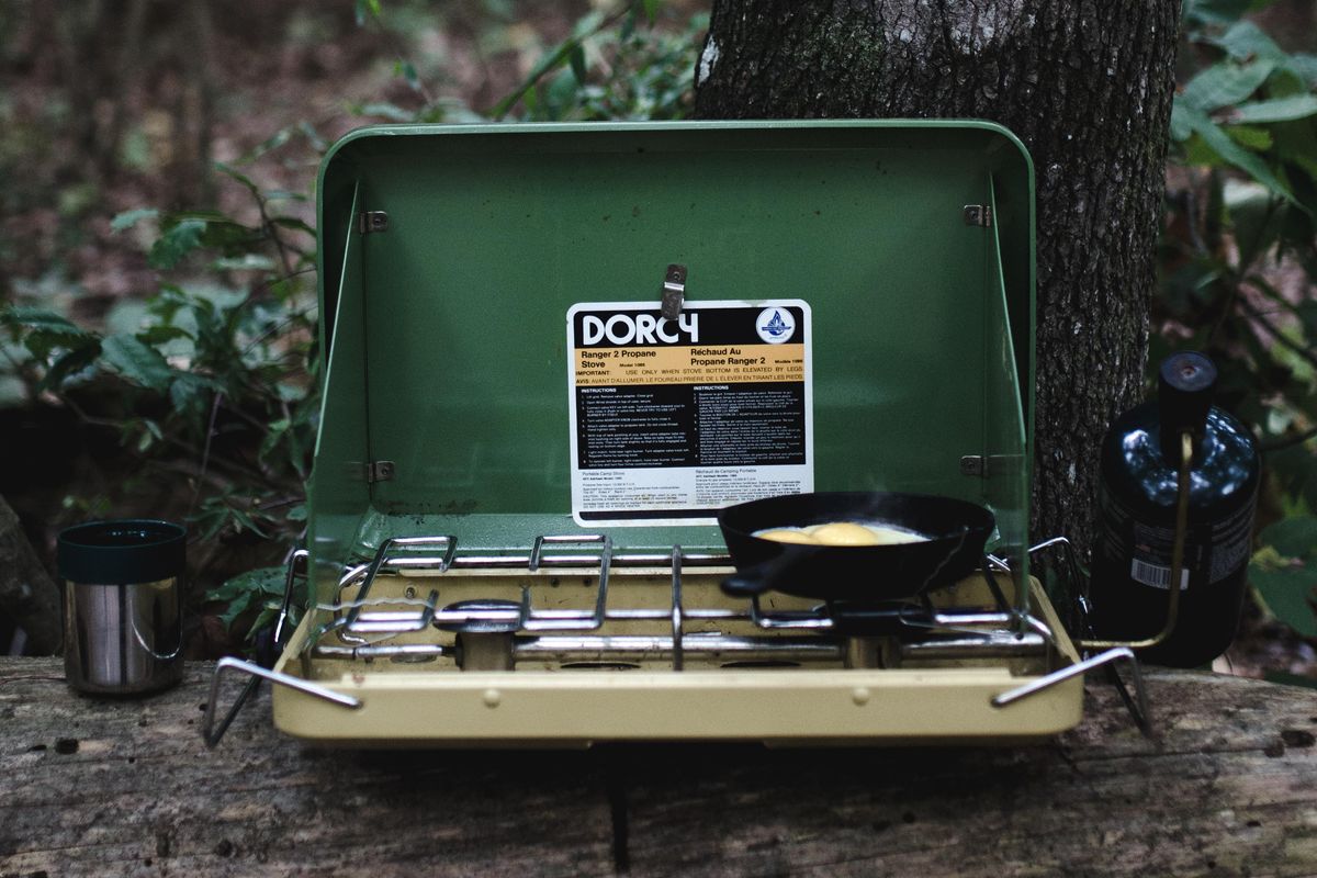 selective focus photography of camping stove on lug with cooked egg on pan.