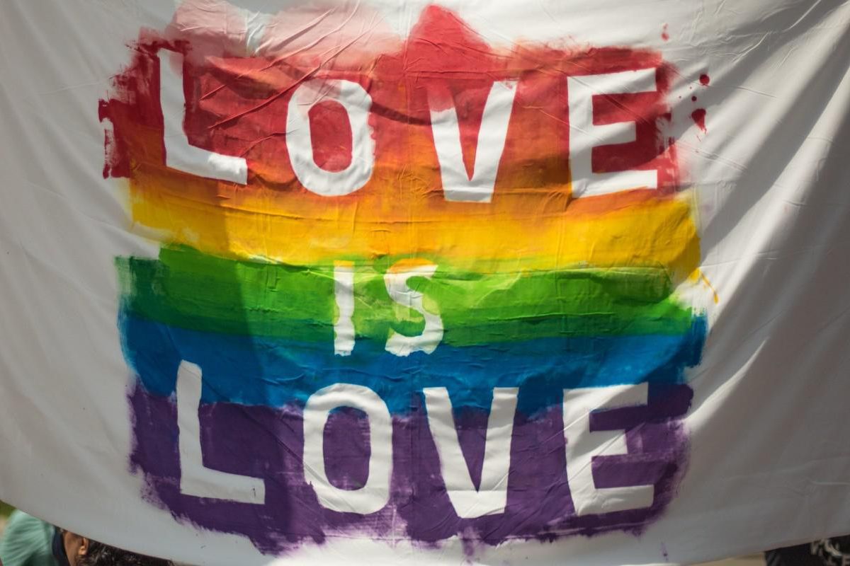 The words love is love are written in white against a painted pride flag.
