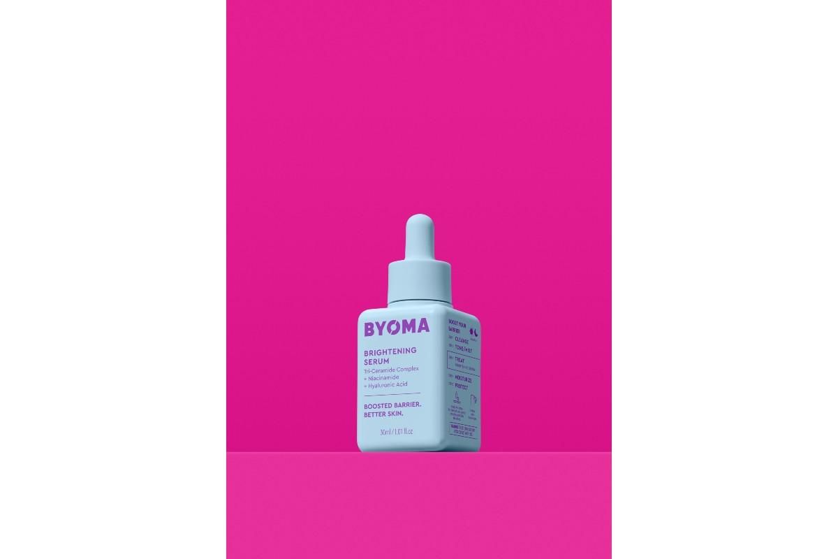 Blue bottle of BYOMA Brightening Serum against a pink background.