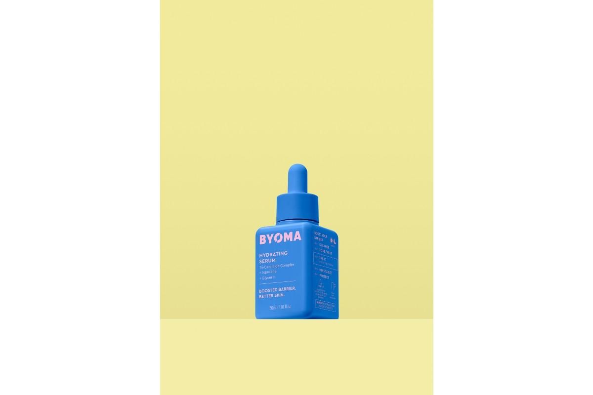 Blue bottle of BYOMA Hydrating Serum against a yellow background.