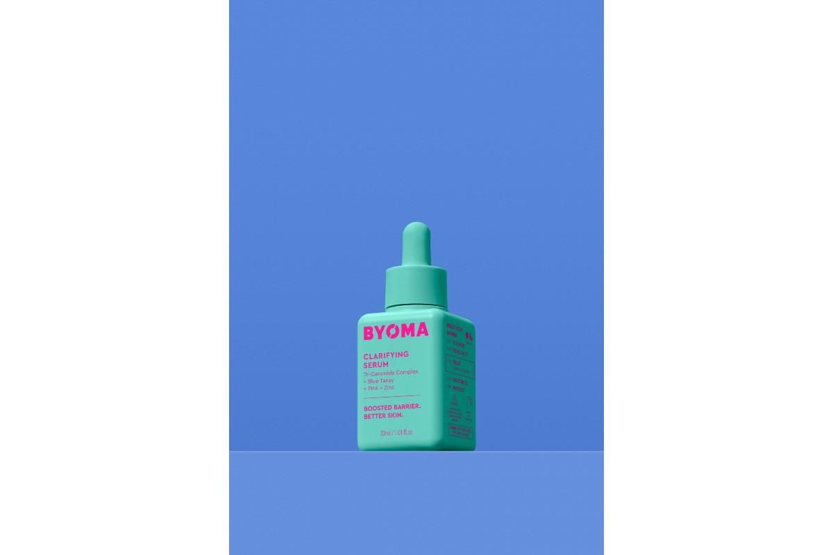 Green bottle of BYOMA Clarifying Serum agains a blue background.
