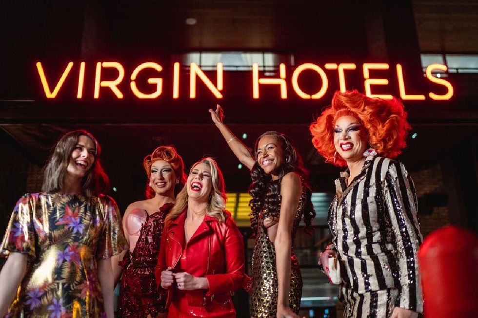 women and drag queens posing and laughing under the virgin hotels neon sign.