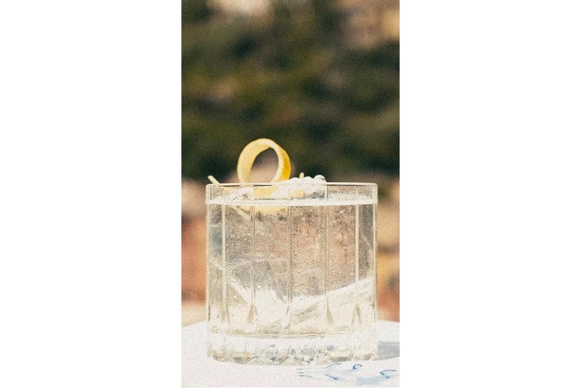 Negroni Bianco in a rocks glass and garnished with a lemon peel sitting on a table outside.