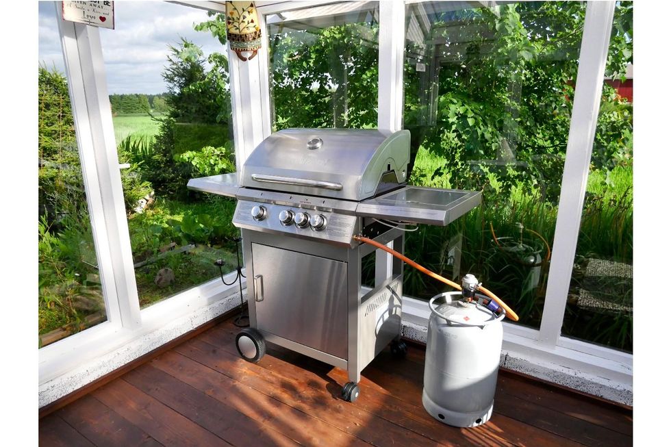 stainless steel gas grill attached to a propane tank on an outside deck.