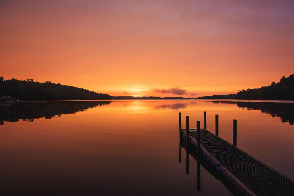a dock jetting out onto a calm lake as the sun sets.