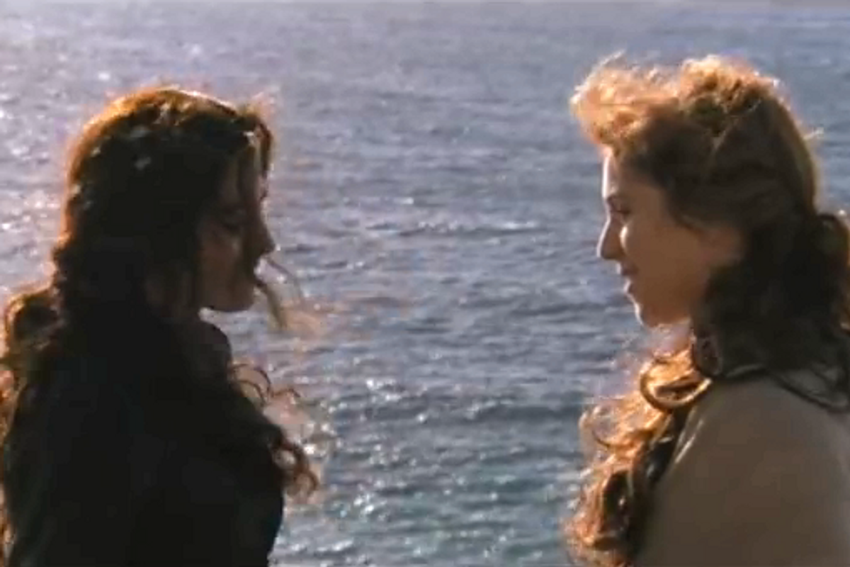 two women with long hair speaking to each other next to a body of water.
