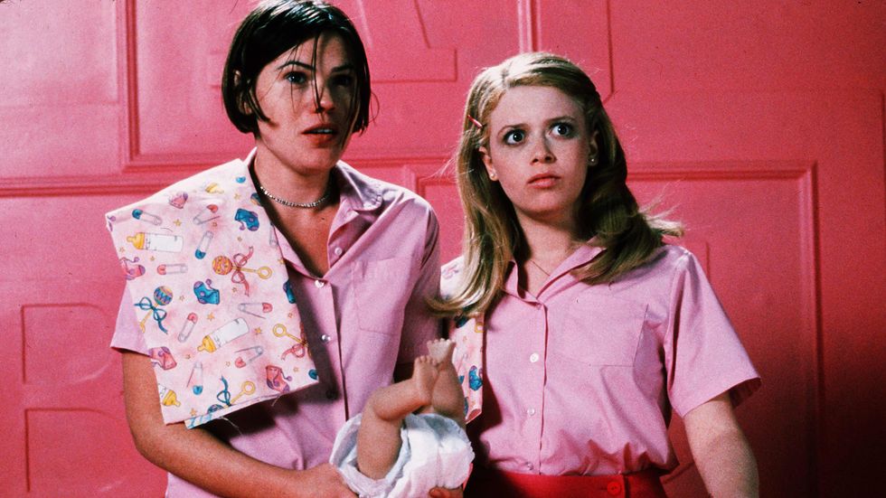 two women dressed in pink look scared while standing in front of a pink wall.
