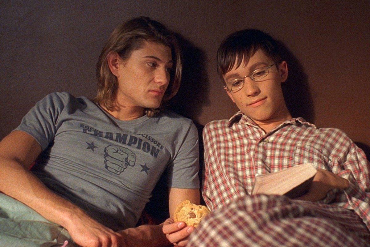 two highschool boys sitting in bed talking.
