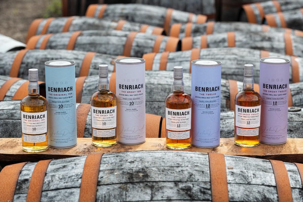 bottles of Benriach scotch whisky lined up on a table with whisky barrels laying in front of them.