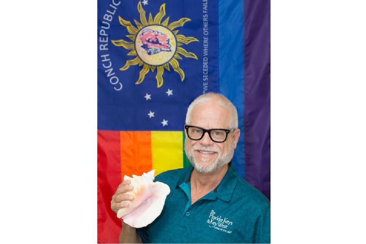 Pony Charvet holding a conch shell in front of an LGBTQ+ flag.