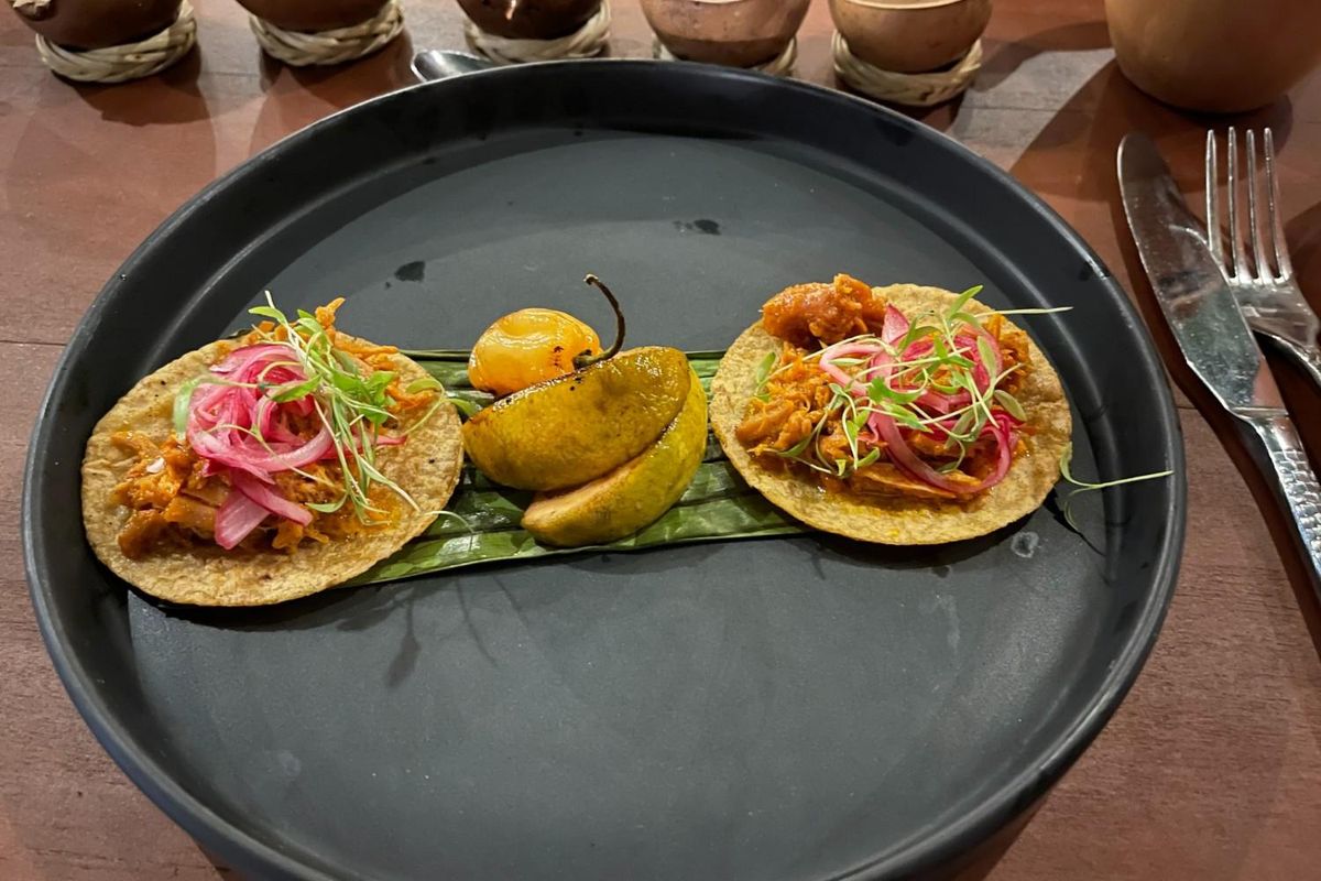two tacos on a black ceramic plate with a roasted habanero and grilled orange wedges.