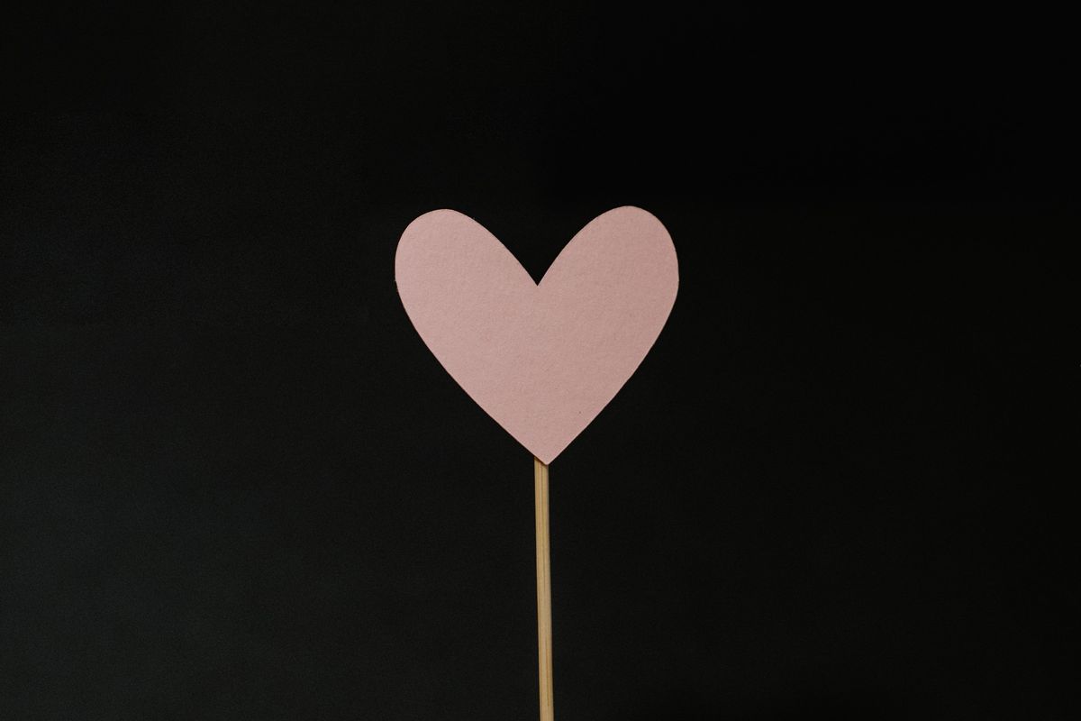A pink paper heart on a stick with a black background.