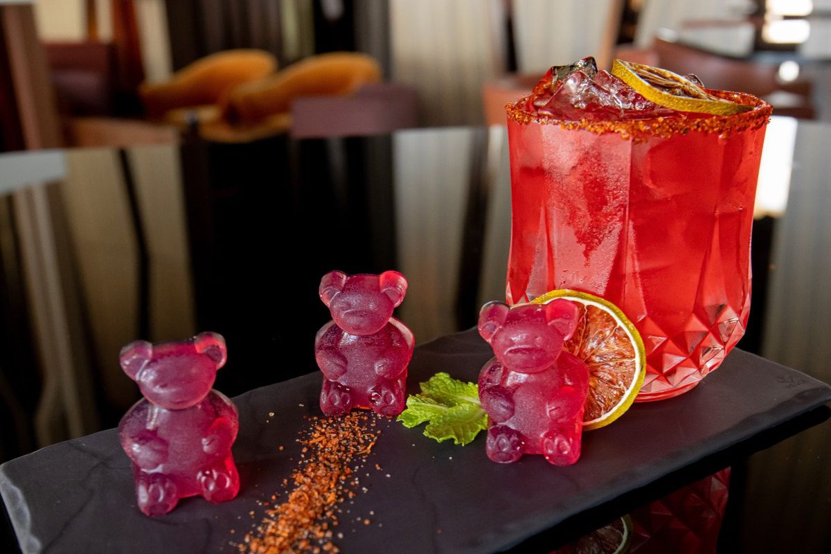 three red gummy bears sitting next to a red margarita.