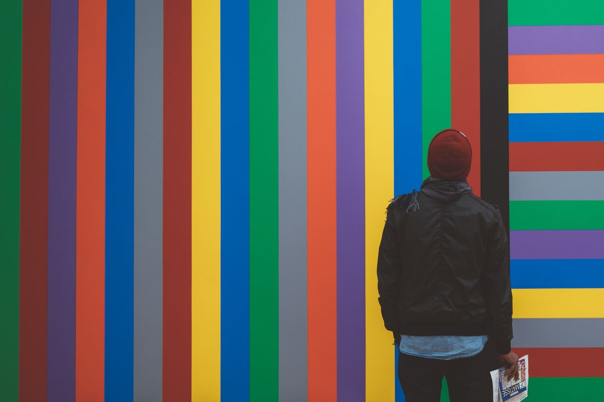 A man standing in front of a rainbow colored art piece.