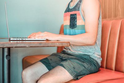 man in blue and red tank top and blue denim shorts sitting on brown wooden chair.