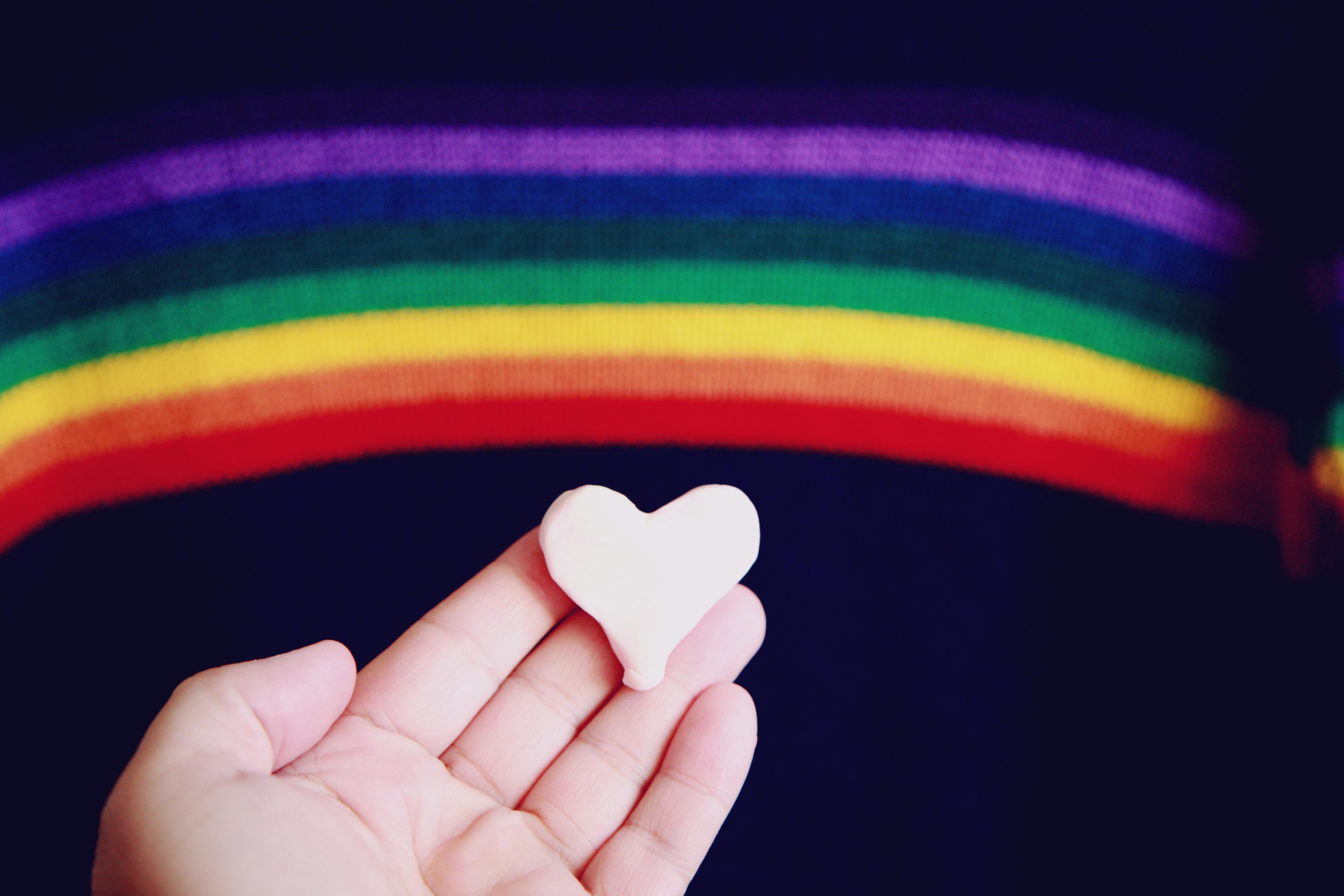 person holding a heart underneath a rainbow