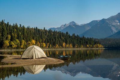 white tent on lake near green trees and mountain under blue sky during daytime.