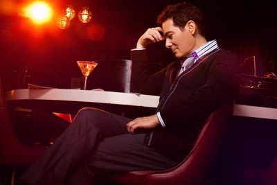 Michael Feinstein sitting at table in reflective pose with a martini. 