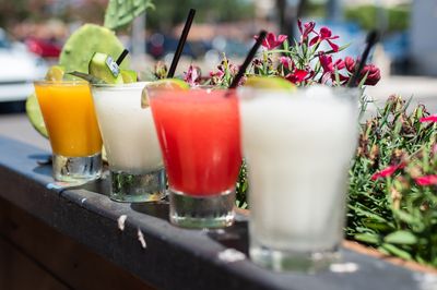 four different margarita drinks sitting outside on the ledge of a flower box.