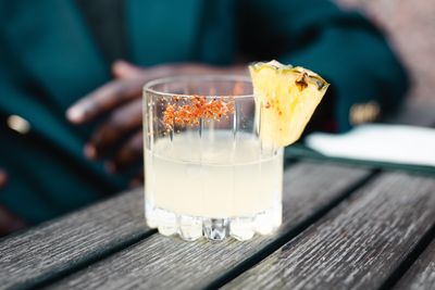 tequila cocktail with tajin and pineapple wedge on the rim sitting on a wood slat table.