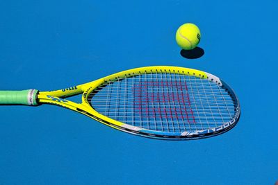 yellow Wilson tennis racket and tennis ball sitting on a blue tennis court.