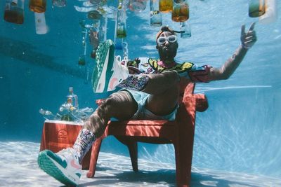 Man sitting in a lawn chair next to cocktails underwater.